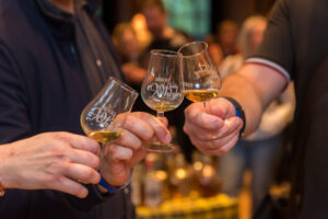 Ein Close-up Foto zeigt drei Hände, die in der Mitte des Bildes nebeneinander drei Glencairn-ähnliche Whisky-Tasting-Gläser halten.