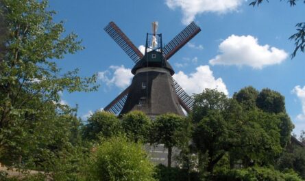 In der Mitte des Bildes ist die Windmühle Johanna zu sehen. Im Vordergrund sind grüne Bäume zu sehen. Im Hintergrund ist blauer Himmel mit Wolken. Foto: Spudaitis bei Pixabay