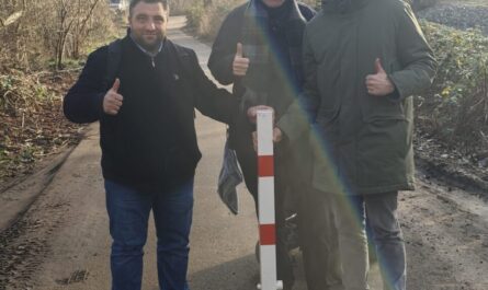 Drei Aktive stehen hinter dem neuen rot-weiß geringelten Poller auf einem Weg im Kleingartenverein.