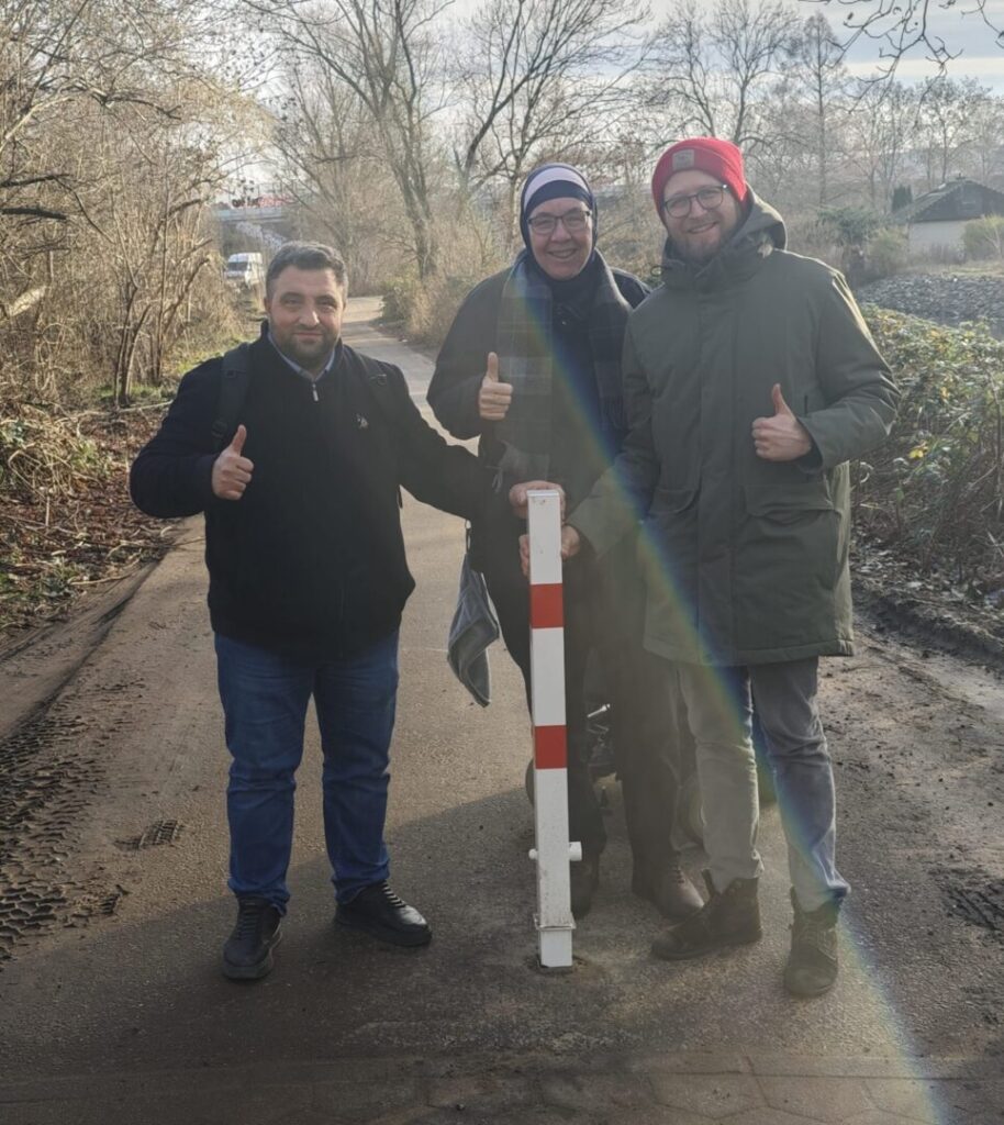 Drei Aktive stehen hinter dem neuen rot-weiß geringelten Poller auf einem Weg im Kleingartenverein.