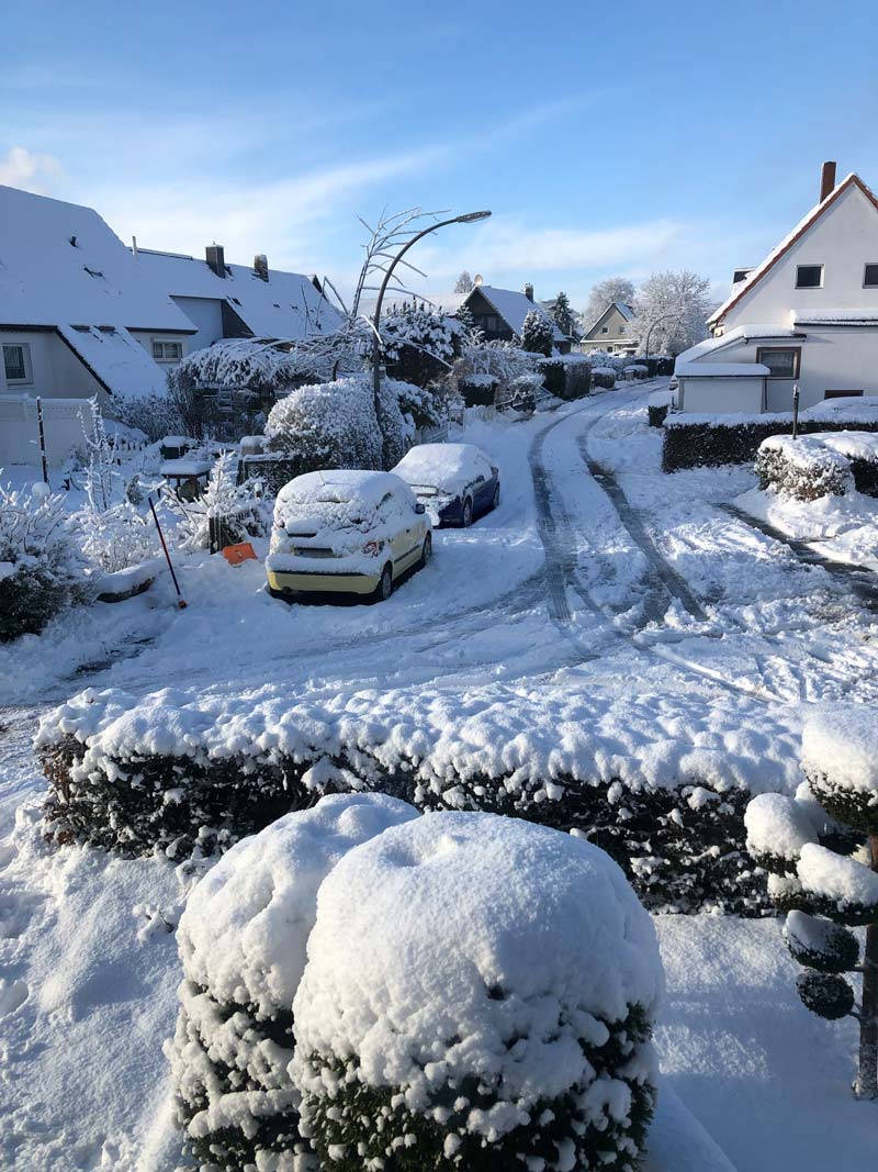 Blick vom Kopf einer Sackgasse in einer Wohnstraße mit kleinen Doppelhäusern im Schnee. Die Straße ist vereist mit Spurrillen. Die Sonne scheint.