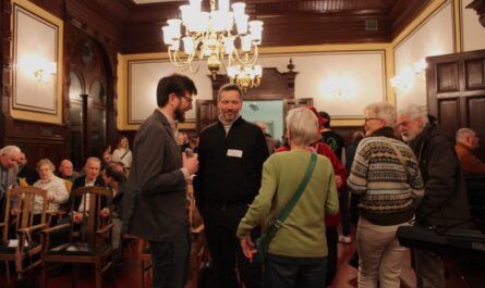 Verschiedene Menschen im Ratssaal unter einem Kronleuchter. Foto M. Brito