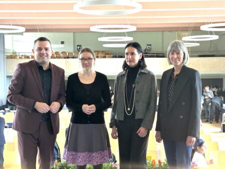 Links ein Mann, daneben drei Frauen. die zweite Frau in einem Glockenrock. Über den menschen eine Decke mit runden Leuchten.