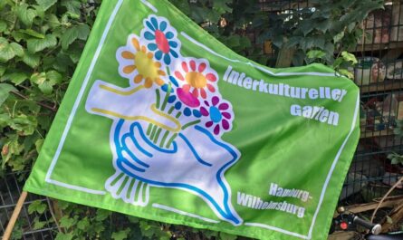 Stofffahne mit der Illustration des Interkulturellen Gartens: Aus der Kontur der Elbinsel wächste eine Hand, die mit einer zweiten Hand einen bunten Blumenstraße hält. Auf leuchtend hellgrünem Grund.