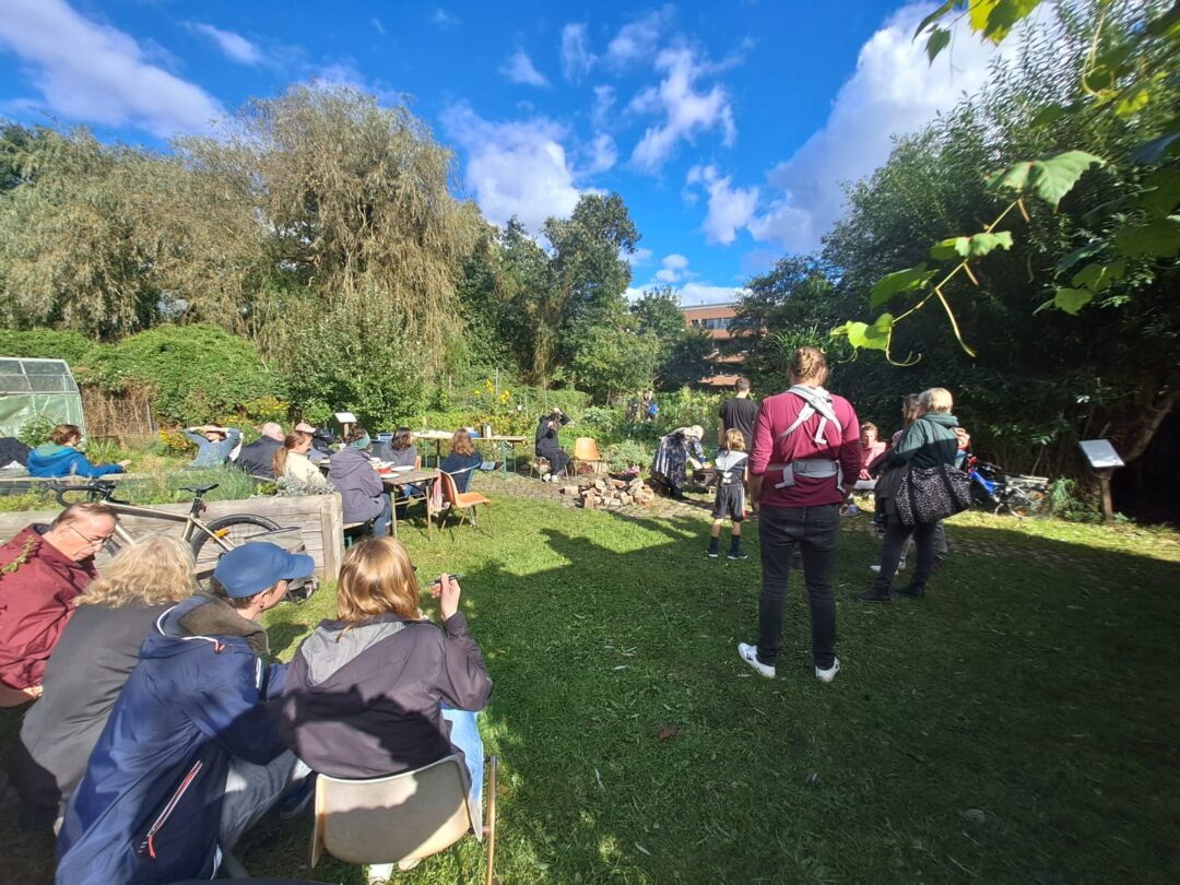 Im Garten, Vereinsmitglieder und Besucherinnen sitzen und stehen zusammen in der Sonne Foto: Interk. Garten
