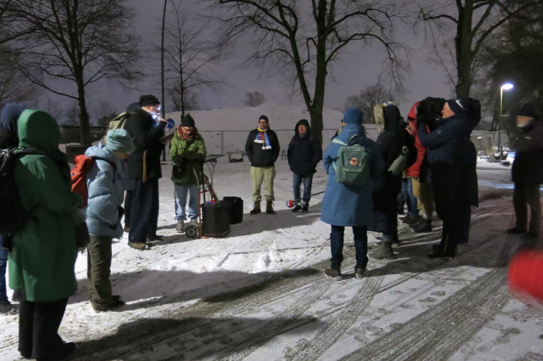 Die Gruppe steht im Kreis im Schnee. Oliver Menk liest vor