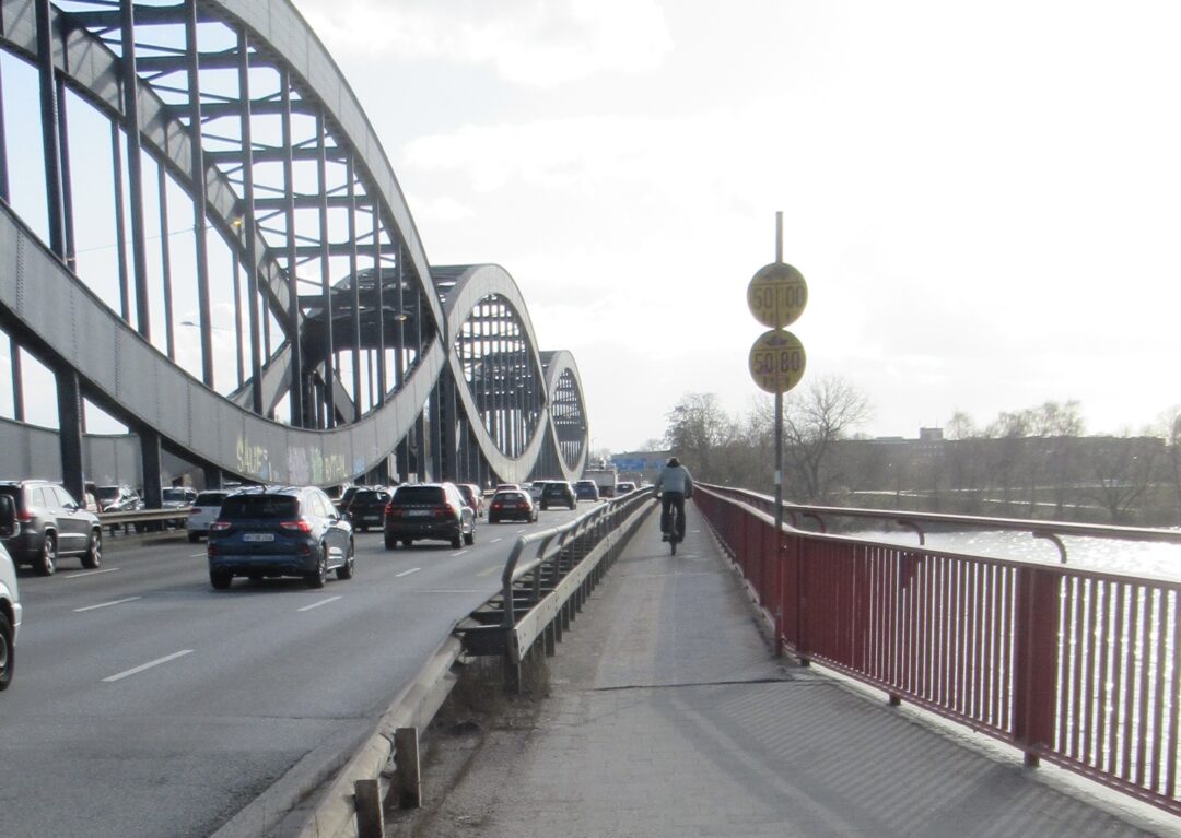 Blick auf die Neue Elbbrücke mit viel Autoverkehr und rechts daneben der schmale Radweg mit Fahrradfahrer 