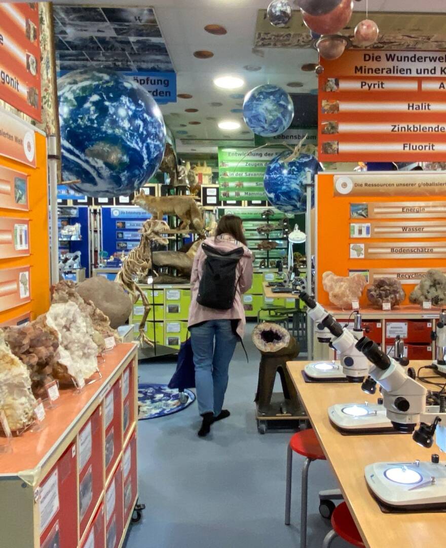 Blick in einen Gang des Museums. An der Decke drei blaue Erdkugeln. Rechts, links und hinten Exponate. Inder Mitte eine Frau mit Rucksack. Rechts sieht man zwei Mikroskope.