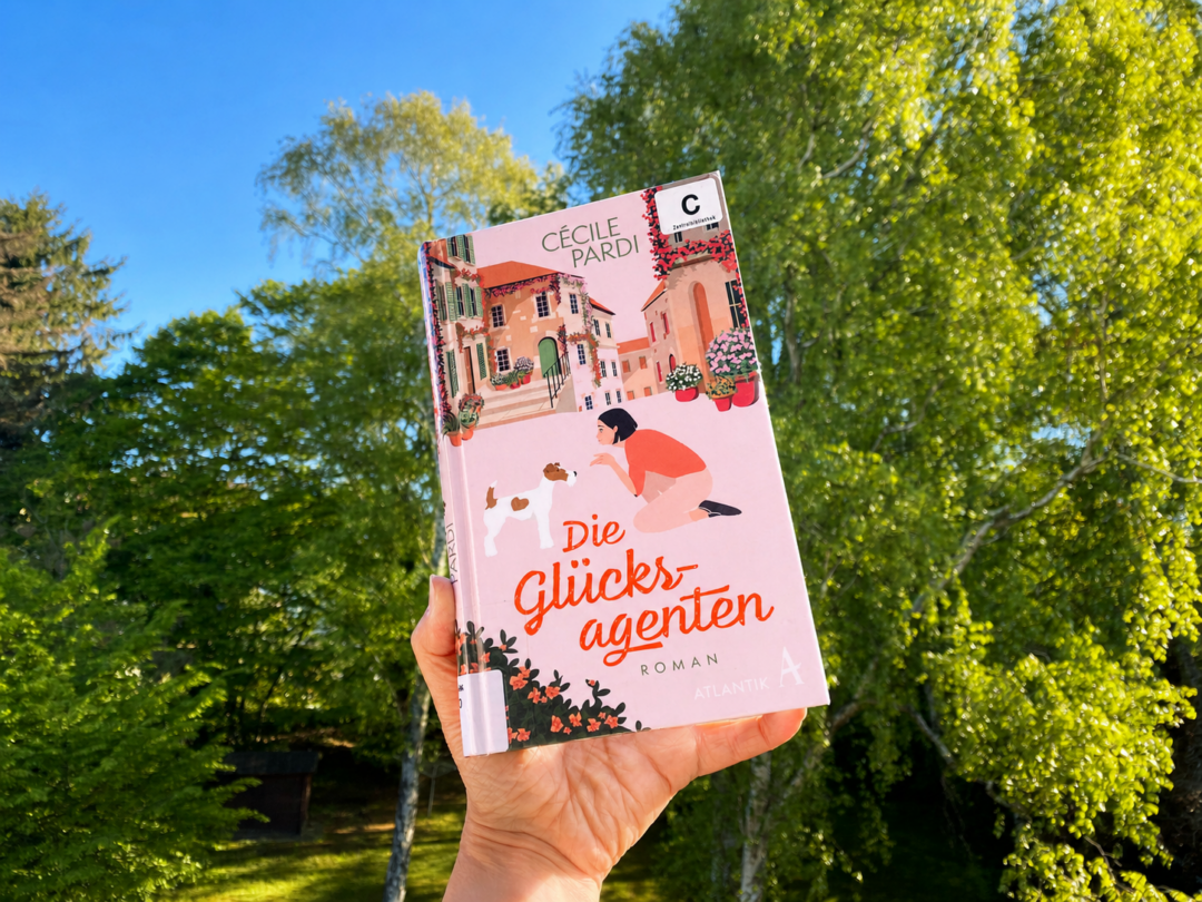 Eine Hand hält das Buch. Im Hintergrund Bäume und eine Wiese. Foto: Meret Büchner