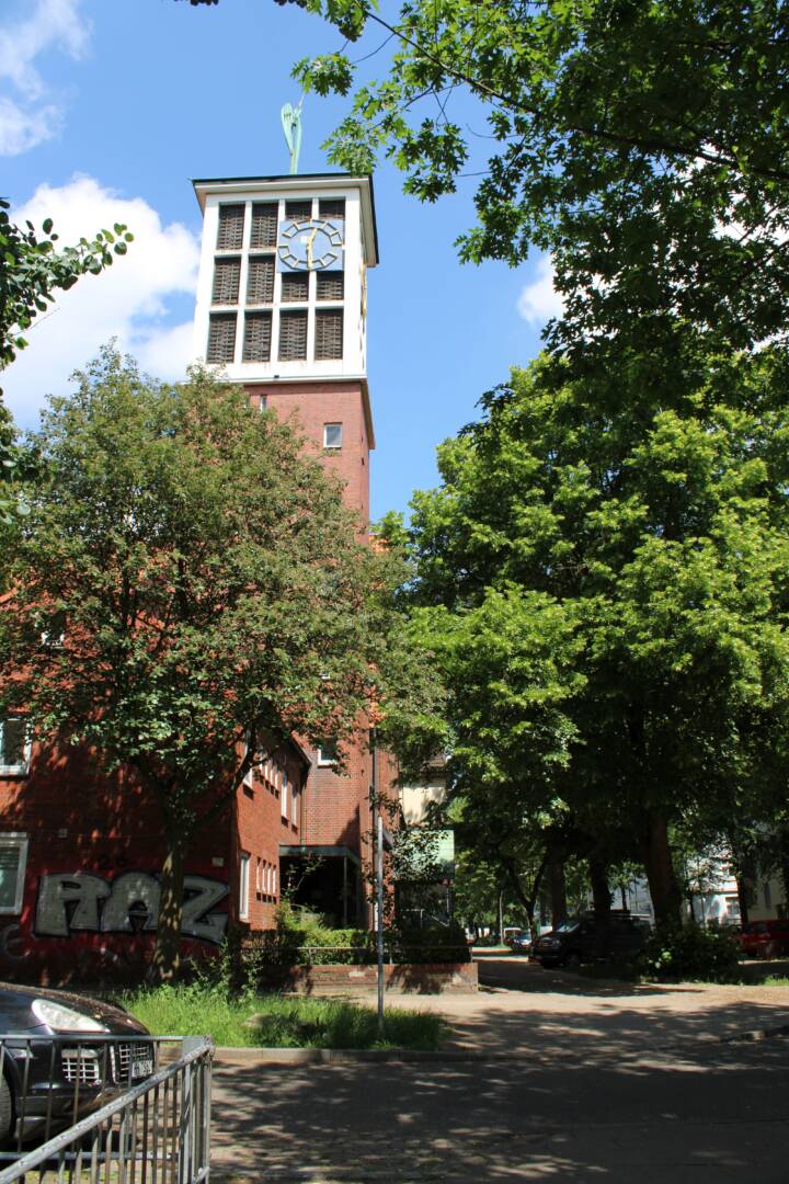 Hinter Bräumen im Vordergrund steht ein Kirchturm. Der obere Teil besteht aus Fenstern mit weißen Rahmen.
