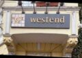 Vor der Ecke eines gelben Gründerhauses, unter dem grauen Schild westend,. stehen vier Menschen. Außen zwei Frauen und in der Mitte zwei Männer.