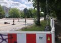 Im Vordergrund (und auch weiter hinten) überall rot-weiße Baustellen-Absperrungen. Dazwischen eine leer Straße. Im Hintergrund Hochhäuser. Links und rechts der Straße Grünstreifen mit grünen Bäumen Foto: Marianne Groß