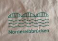 Jutebeutel bedruckt mit einer drei bogigen Brücke, darunter Wellen und der Schriftzug Norderelbbrücke. Foto: Thomas Bohn