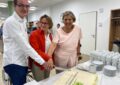 Ein Mann und zwei Frauen stehen hinter einer Marzipantorte mit einem Kuchenmesser in den drei Händen, die sich anfassen.