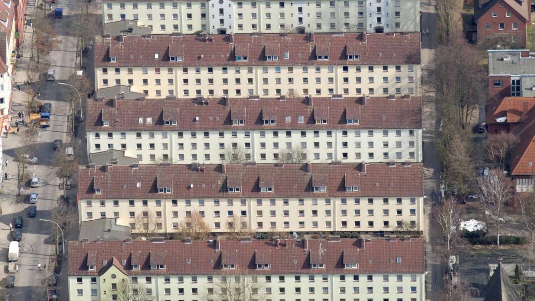Luftaufnahme von 5 nahezu identischen Häuserriegeln: Die Häuser sind weiß mit roten Ziegeldächern, 3stöckig plus Dachwohnungen. Vermutlich je 4 Eingänge, mit je 8 Wohnungen. Foto: ????