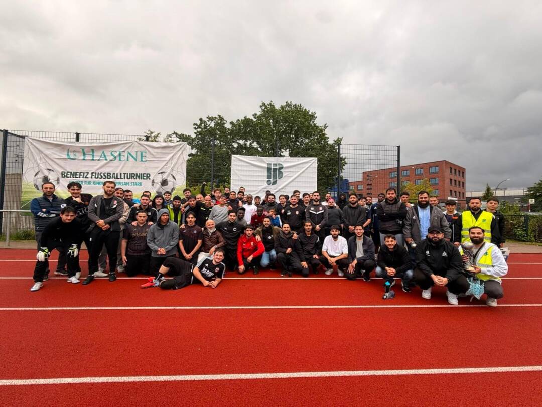 Auf einem Sportplatz mit rotem Untergrund sitzen, liegen stehen alle Beteiligten des Cups in einem großen Halbkreis vor zwei Bannern auf denen der Name des Turniers und das Logo des IJB abgebildet sind. Foto: Mustafa Kocak