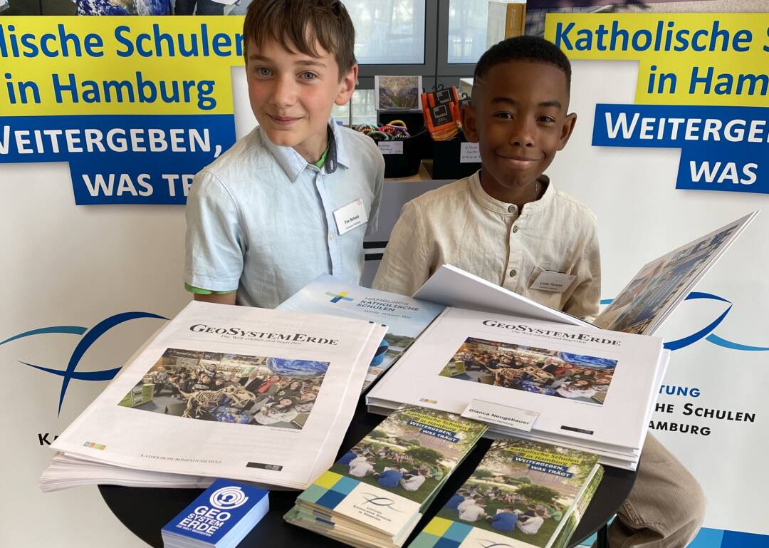 Ein weißer Junge und ein schwarzer Junge sitzen hinter aufgeschlagenen großen Büchern.