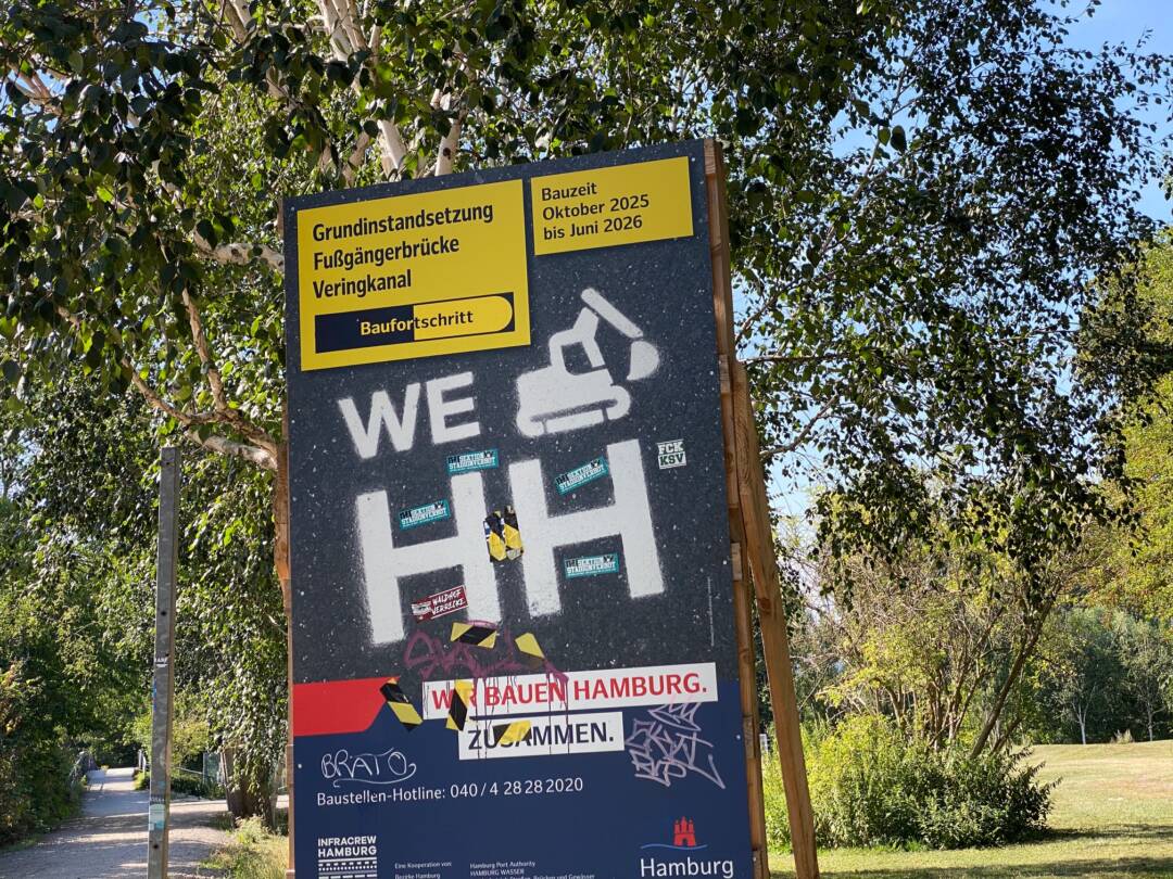 Vor grünem Laub steht ein Baustellenschild von Hamburg