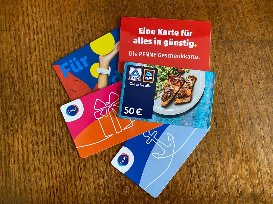 Auf einer Holzplatte liegen 5 Gutschein-/Geschenkkarten von versch. Geschäften