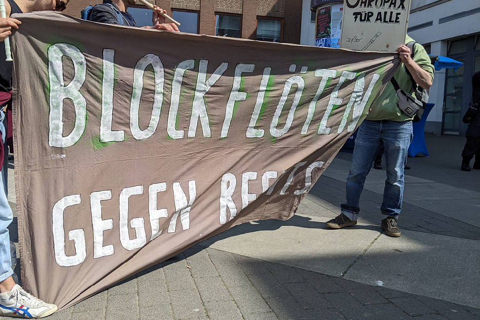 Zwei Demonstranten halten ein braunes Transparent mit weißer Aufschrift: Blockflöten gegen Rechts