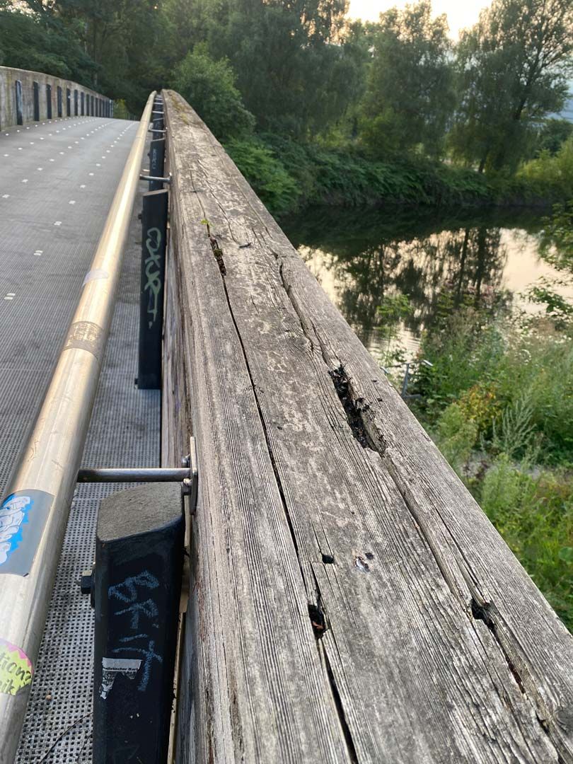 Das Holzgeländer einer Fußgängerbrücke.