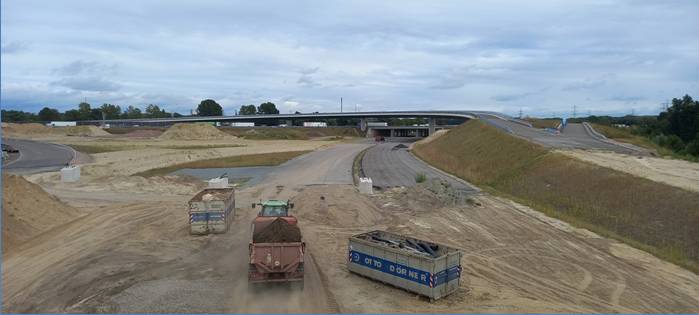 Riesiges Straßenbaugelände. Im Hintergrund eine Brücke. Im Vordergrund zwei Container und ein Trecker.