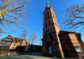 Ein künstlerisches Foto mit stark „stürzenden Linien“. Im Zentrum steht der Turm von St. Emmaus. Der Himmel ist strahlend blau, die Bäume links und rechts haben keine Blätter (Winter). Foto: Lars Meyer