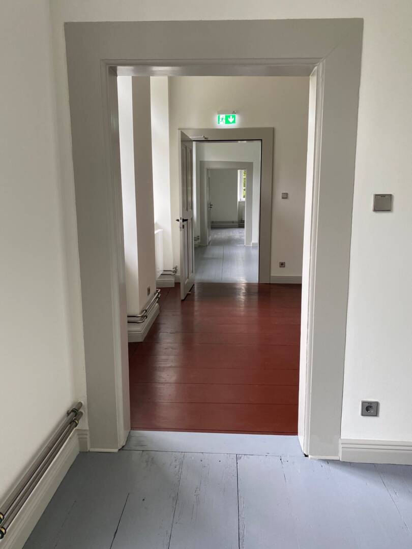 Mehrere Türöffnungen mit grauen Zargen. Vorne grauer Bretterfußboden und im zweiten Zimmer brauner Fußboden.