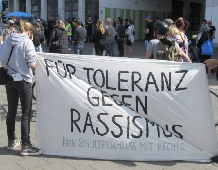 Demonstration, im Vordergrund ein großes Transaparent mt der Aufschrift Für Toleranz gegen Rassismus (schwaze Schrift auf weiß)