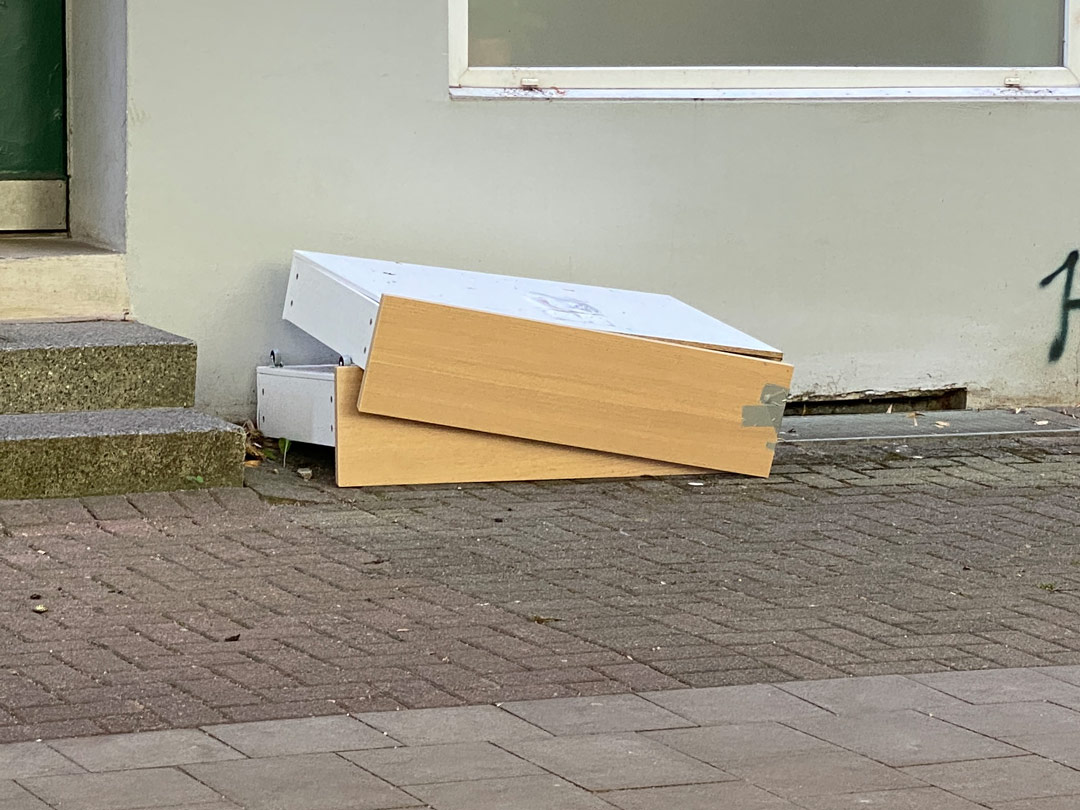 Vor einem Hauseingang in der Veringstraße liegen zwei große Schubladen aus billigen Pressplatten mit Kunststofffurnier.