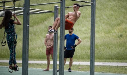 Drei männlich und eine weiblich gelesene Person am und um ein Outdoorfitnessgerät. Im Hintergrund ein Hang/Deich mit Gras Bild von Edmund_H auf Pixabay