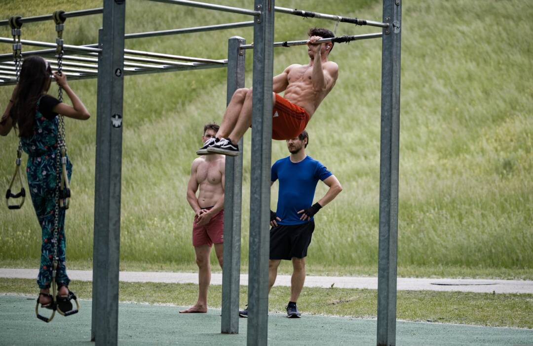 Drei männlich und eine weiblich gelesene Person am und um ein Outdoorfitnessgerät. Im Hintergrund ein Hang/Deich mit Gras Bild von Edmund_H auf Pixabay