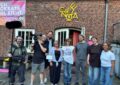 Vor dem Cafe Nova, das in einem alten, urbanen Backsteingebäude untergebracht ist, stehen zwei Männer mit Kamera- und Ton-Equipment, sowie 6 weitere Personen. Alle strahlen in die Kamera