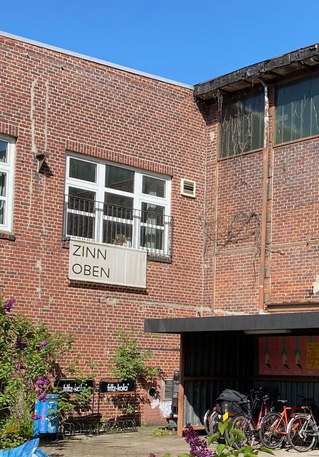Ein Backsteinhaus mit weißem Fenster. Rechts unten sind Fahrräder abgestellt.