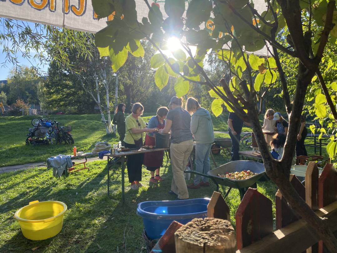 Im Gegenlicht: Auf dem Rasen vor dem Interkulturellen Garten sind Kinder und Erwachsene dabei, von Hand Apfelsaft herzustellen: Waschen, schneiden, häckseln, pressen.