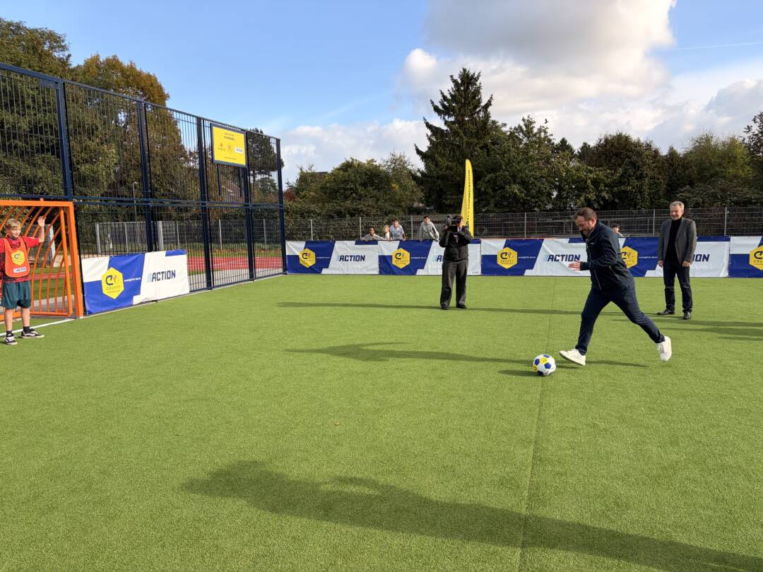 Ein sattgrüner Kunstrasenplatz. Links steht ein Kind im Tor, rechts schießt Van der Vaart einen Ball.