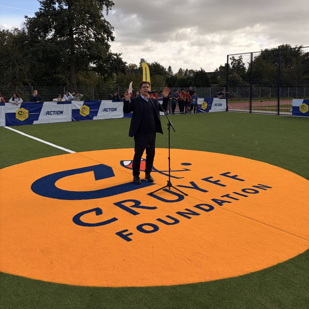 Schulleiter Clasing bei seiner Rede zur Eröffnung des Cruyff Court. Ersteht auf einem riesigen orangen Logo, das im Boden eingelassen ist.