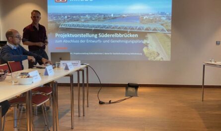 Ein Mann steht links hinter einem Tisch neben dem Eröffnungsbild der Präsentation