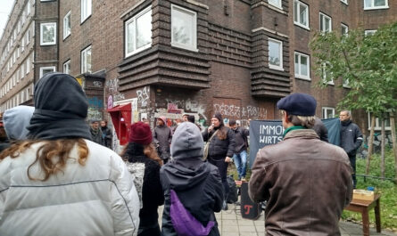 Viele Menschen mit einem Transparent vor einem typischen Veddeler Backstein-Wohnblock.