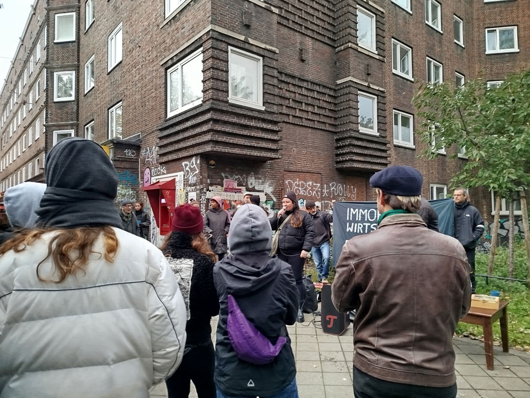 Viele Menschen mit einem Transparent vor einem typischen Veddeler Backstein-Wohnblock.