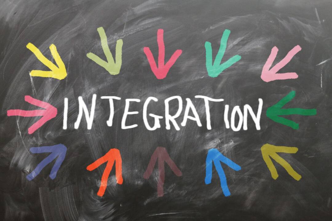 Auf einer anthrazitfarbenen Tafel steht in der Mitte das Wort Integration in Großbuchstaben und weißer Schrift. Im Oval darum herum sind lauter bunte Pfeile gezeichnet.